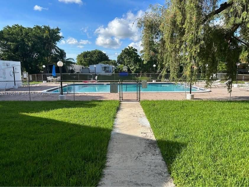 6503 Winfield Boulevard, #211AD, Margate, Margate, FL 33063 In-ground swimming pool surrounded by a concrete deck and enclosed by chain-link fencing, complemented by a manicured lawn and mature trees