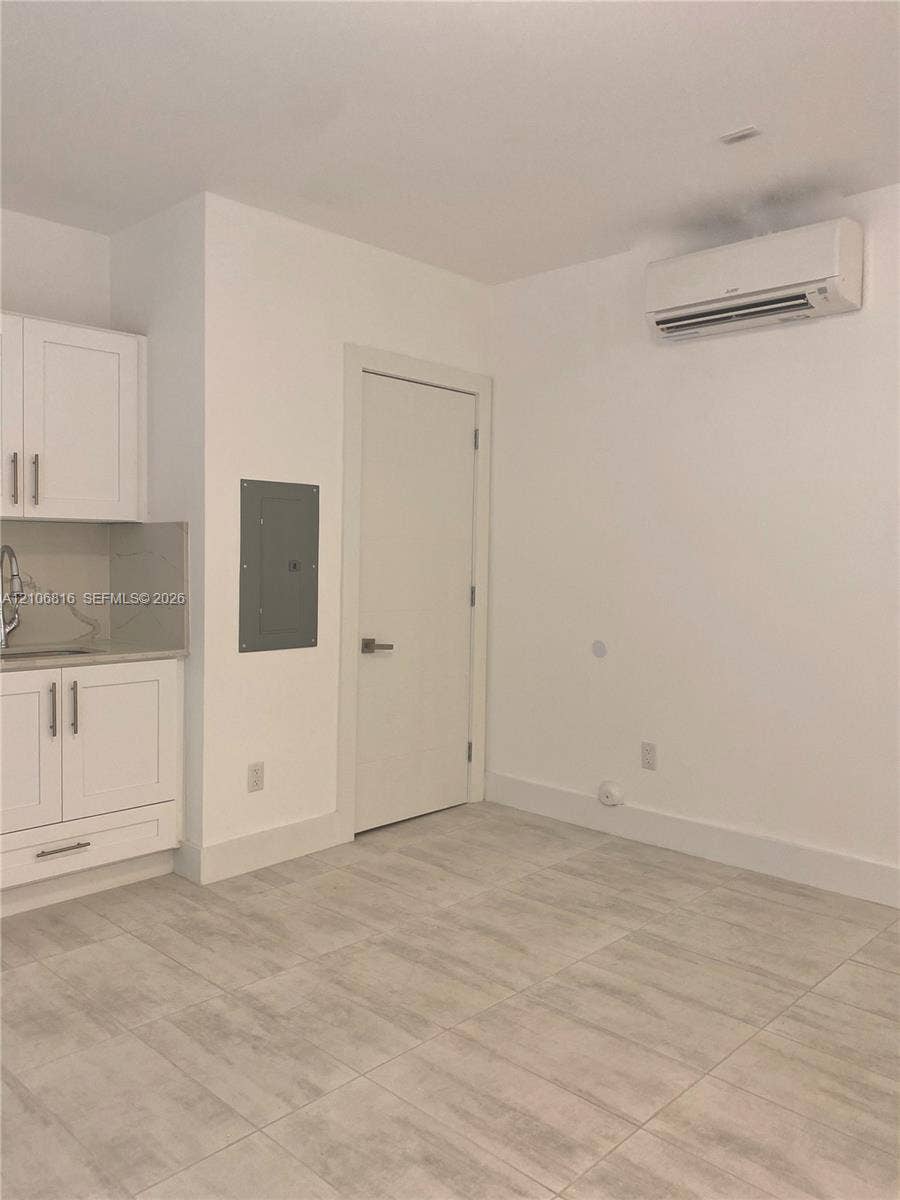 Kitchenette featuring white Shaker-style cabinetry, neutral stone-finish countertops, tile flooring, and wall-mounted air conditioning unit