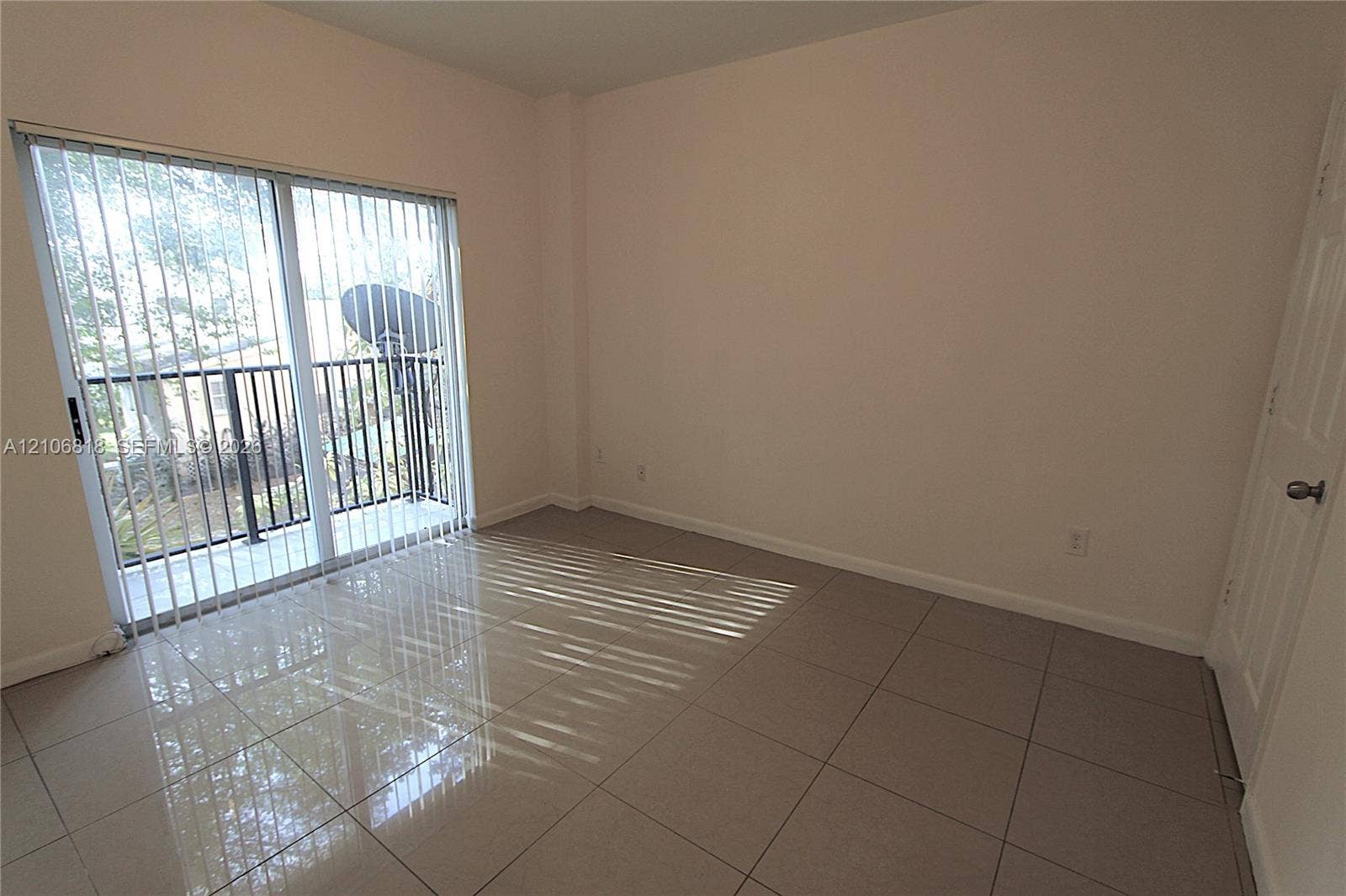 Neutral-toned room featuring large-format polished tile flooring, sliding glass door with vertical blinds, and a private balcony with black metal railing