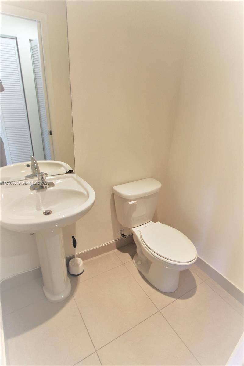 White porcelain pedestal sink with a chrome single-handle faucet, integrated wall-mounted mirror, and tile flooring