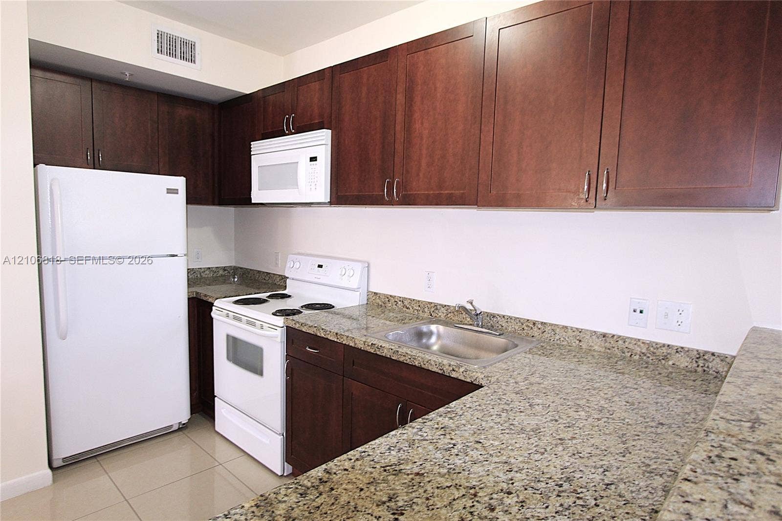 Kitchen featuring wood-finish cabinetry, stone-surface countertops, tile flooring, and white appliances including a range, microwave, and refrigerator