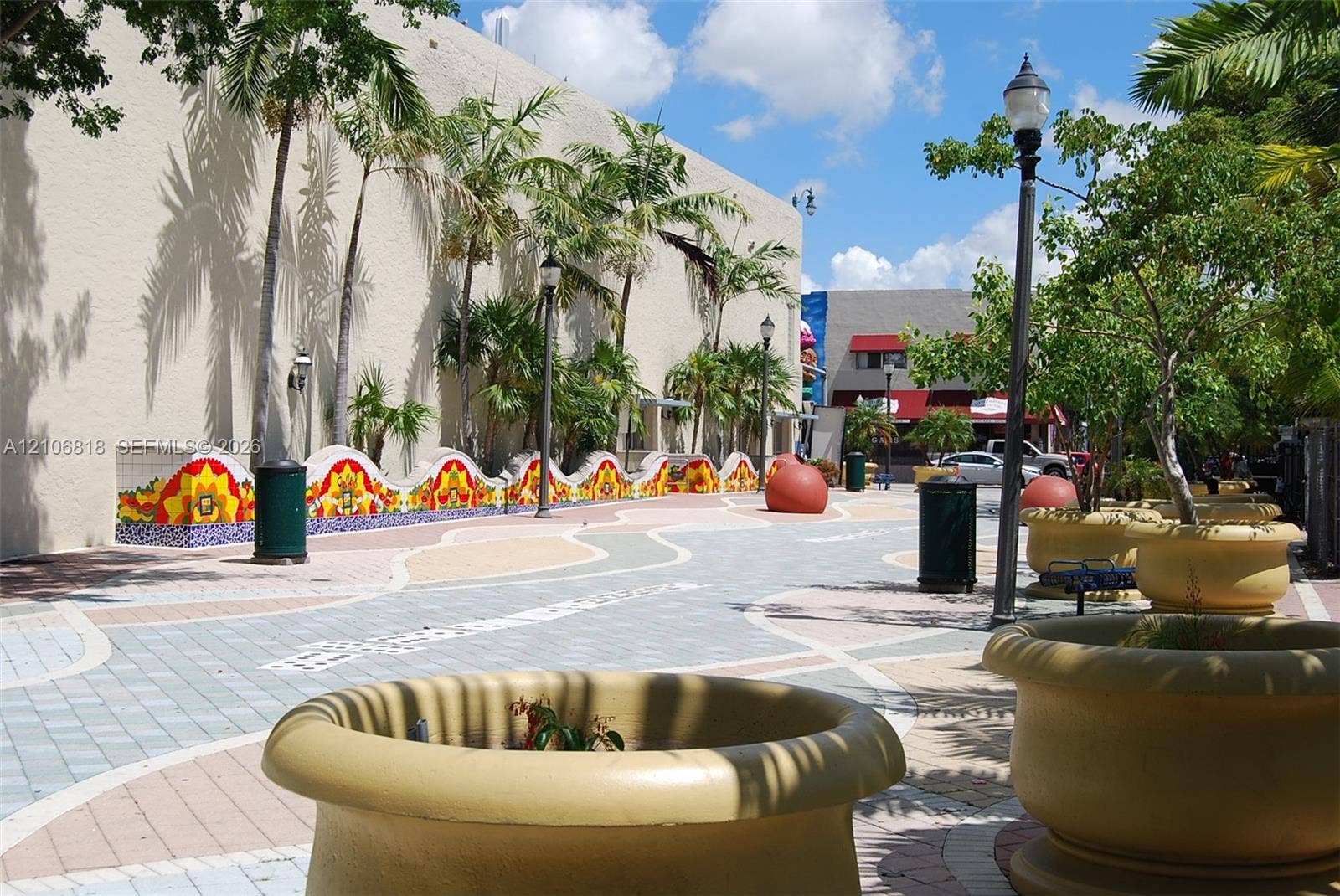 Pedestrian walkway featuring decorative patterned paver stones, vibrant mosaic-tile low walls, mature palm trees, and ornate exterior pedestal-mounted lighting