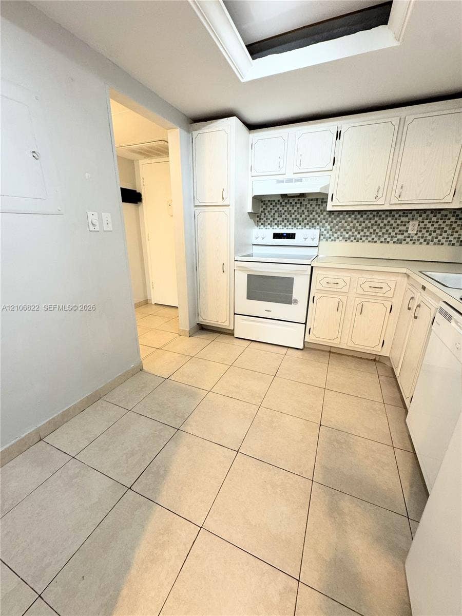 Kitchen featuring white cabinetry, a neutral tile backsplash, built-in range, tile flooring, and a ceiling skylight