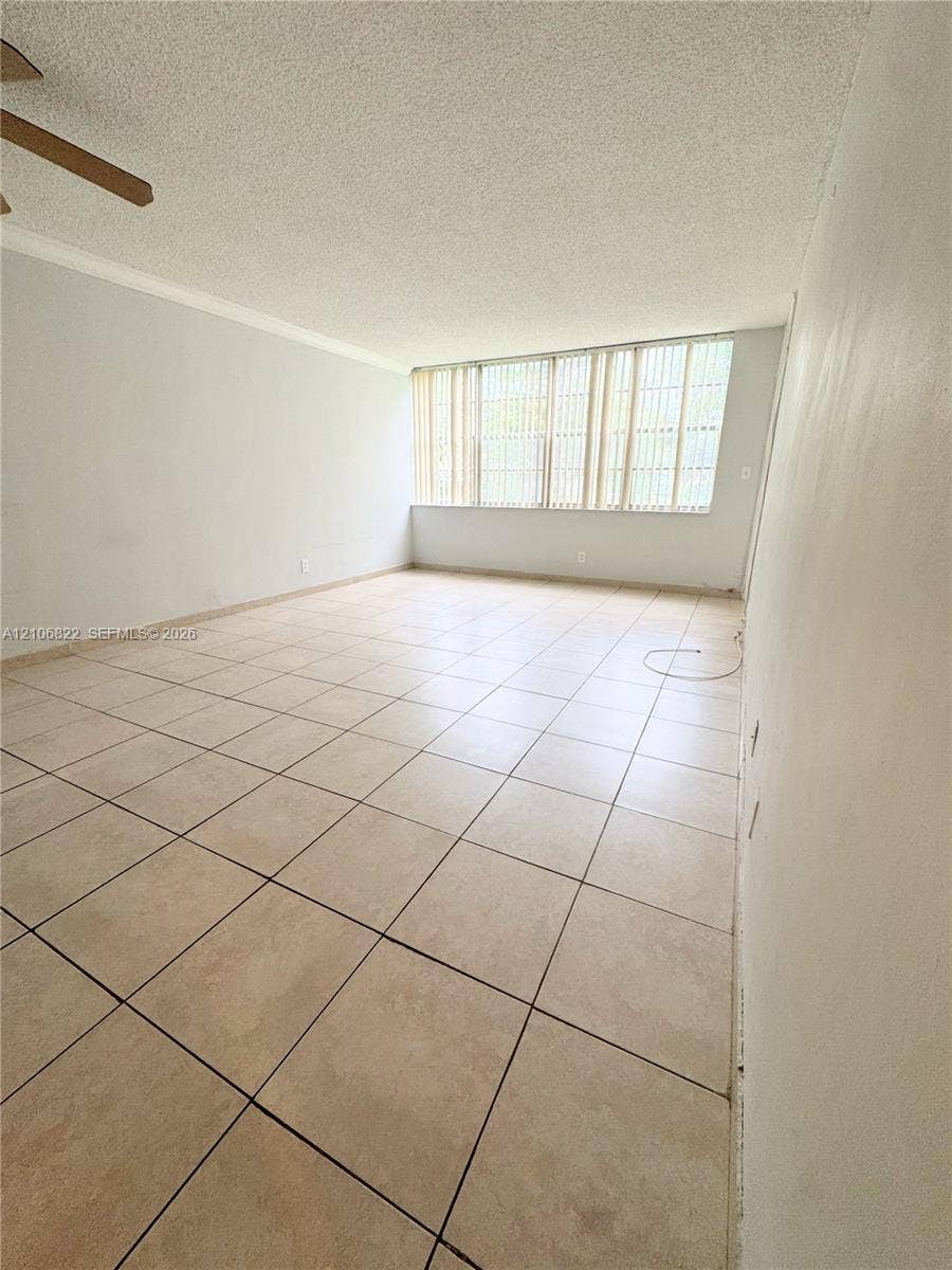 Interior space featuring large-format tile flooring, textured ceiling, and expansive windows with integrated vertical blinds