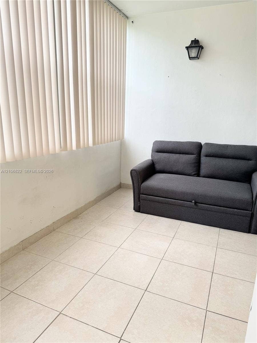 Enclosed area featuring ceramic tile flooring, floor-to-ceiling vertical blinds, and wall-mounted carriage-style lighting