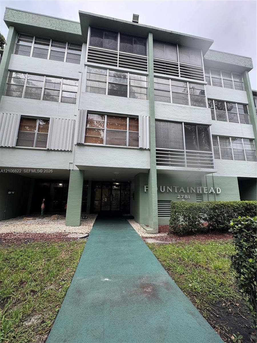 Multi-story residential building exterior featuring a covered entryway, screened balconies, and vertical architectural accents