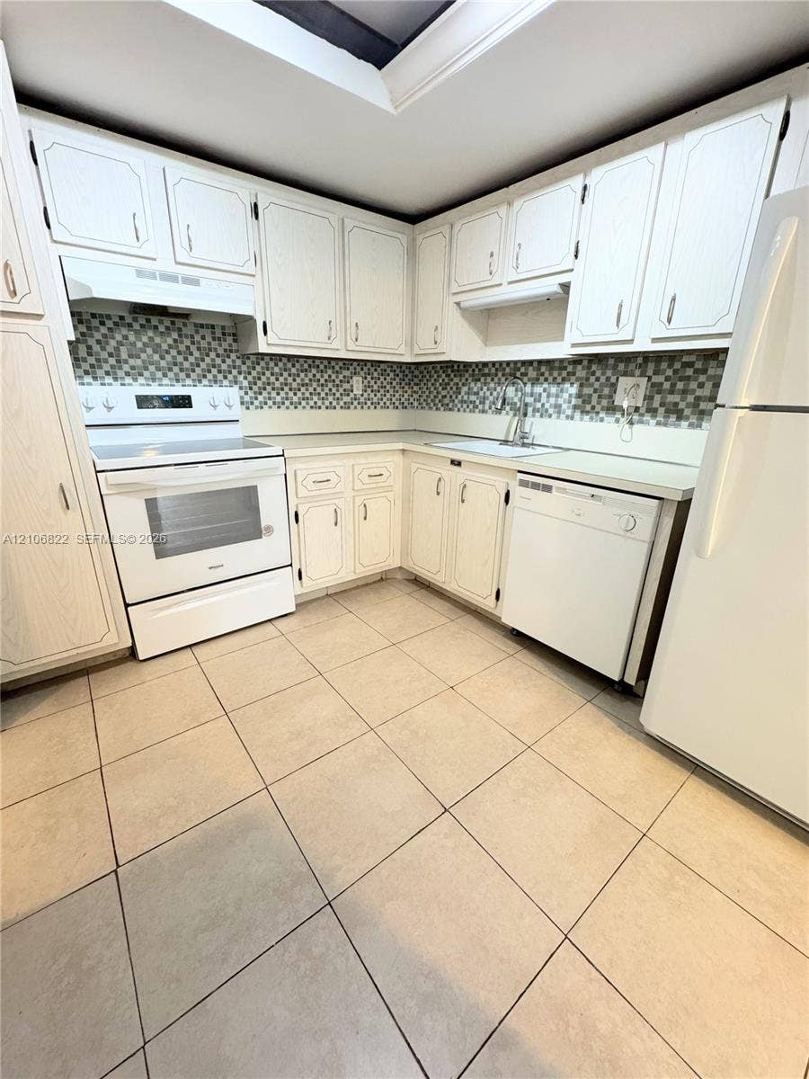 Kitchen featuring white cabinetry, mosaic tile backsplash, solid-surface countertops, tile flooring, and integrated white appliances