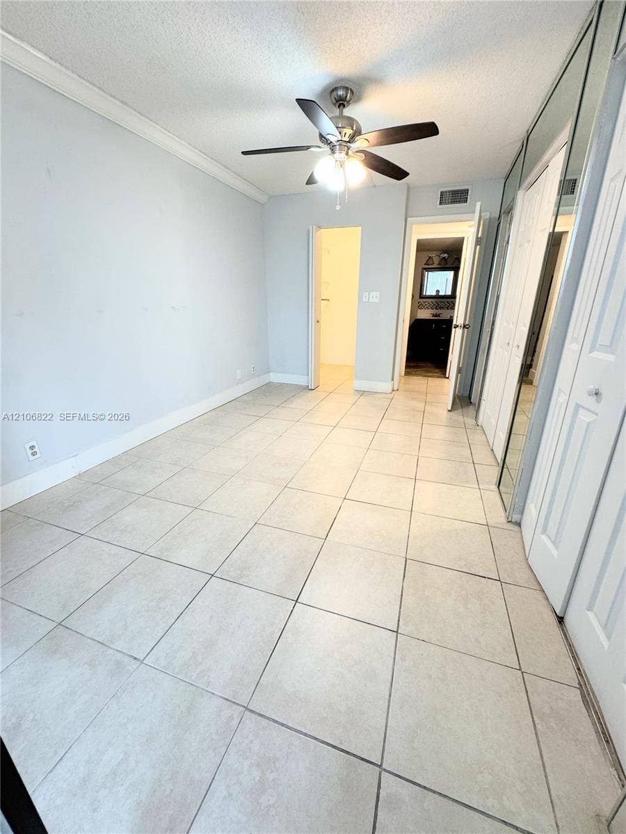 Neutral-toned tile flooring, ceiling fan with integrated light fixture, and floor-to-ceiling mirrored closet doors