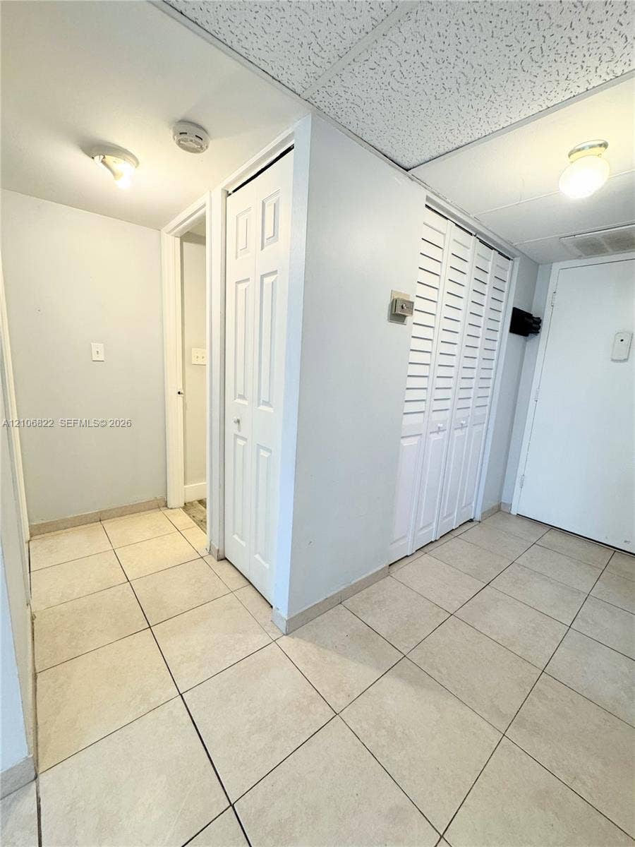 Neutral tile flooring throughout, white louvered bifold closet doors, six-panel interior door, and flush-mount ceiling lighting