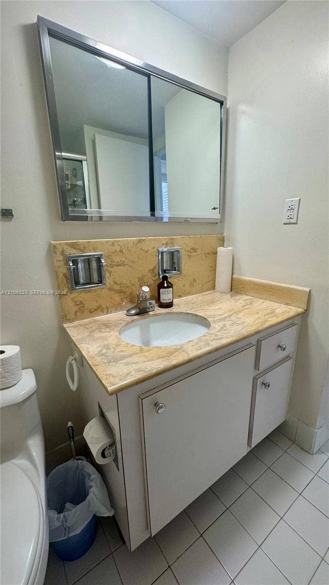 Vanity featuring a stone-patterned countertop, integrated undermount sink, white cabinetry with polished knobs, and a large-format metallic-framed medicine cabinet