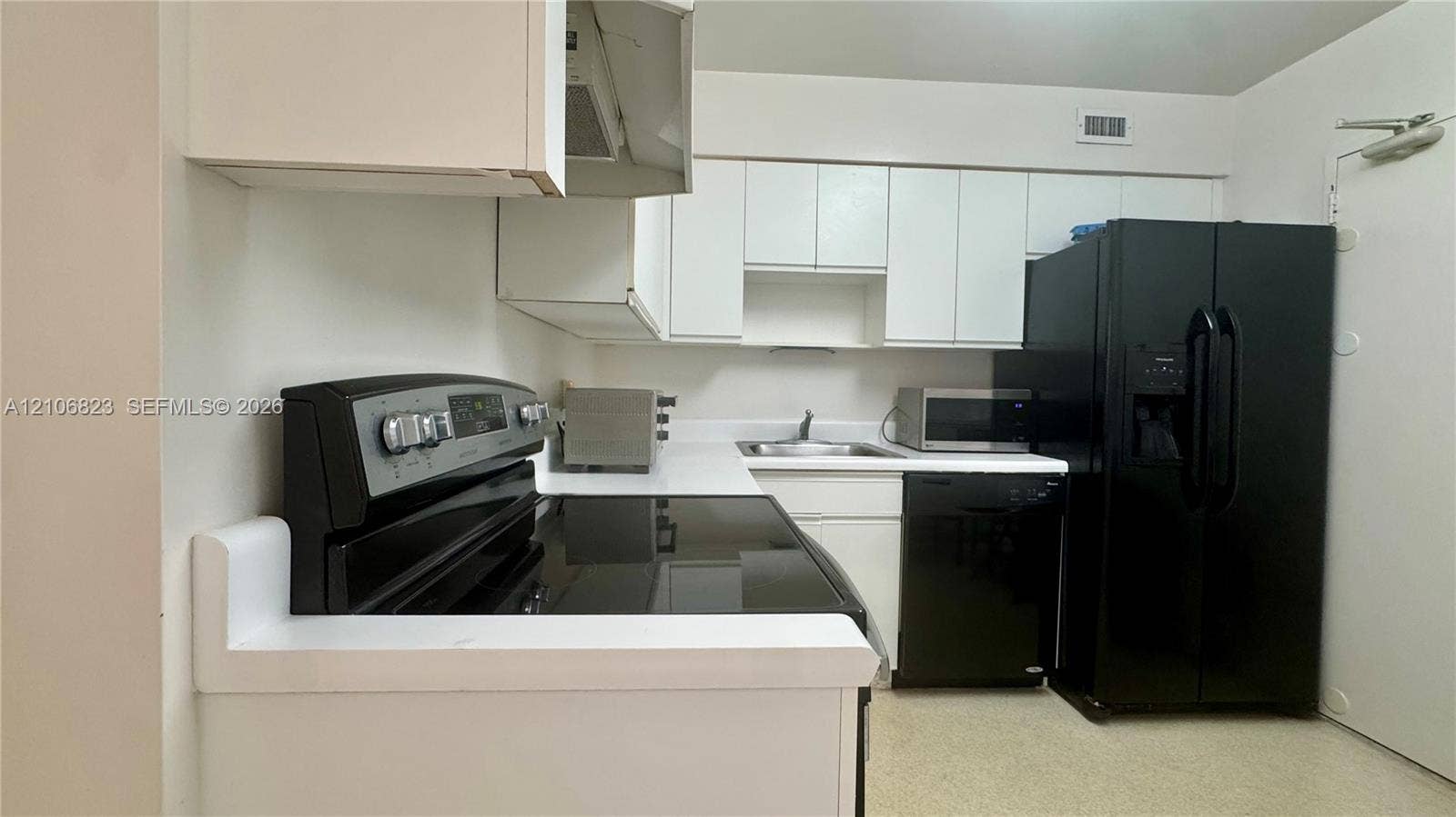 Kitchen featuring white cabinetry, contrasting black appliances, solid-surface countertops, and a dual-basin sink