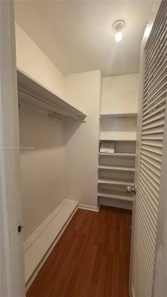 Storage area featuring wood-finish flooring, a built-in hanging rod, multiple fixed shelving units, and a louvered door