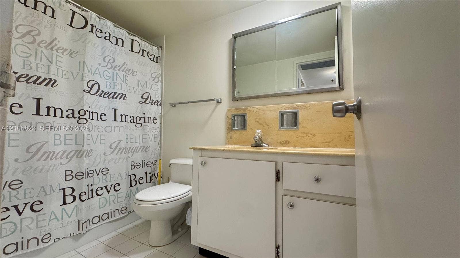 Bathroom featuring a vanity with neutral stone-style countertop, integrated sink, large wall-mounted mirror, and tiled flooring