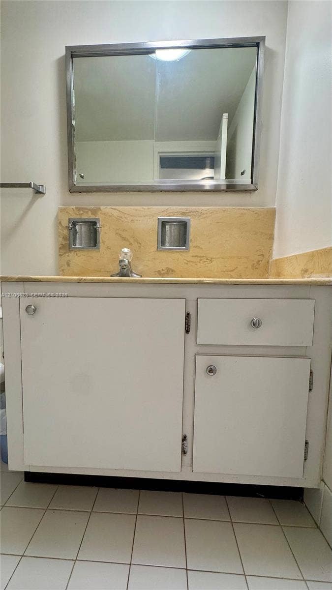 White vanity cabinet with chrome hardware, natural stone countertop with matching backsplash, dual inset soap dishes, and a framed mirror