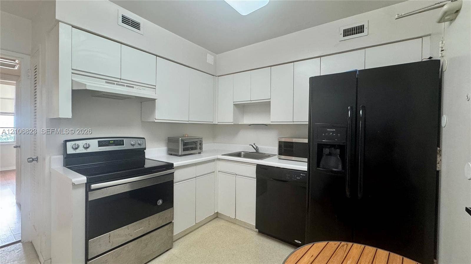 Kitchen featuring white flat-panel cabinetry, solid-surface countertops, integrated range hood, and black appliance suite including a side-by-side refrigerator, dishwasher, and electric range