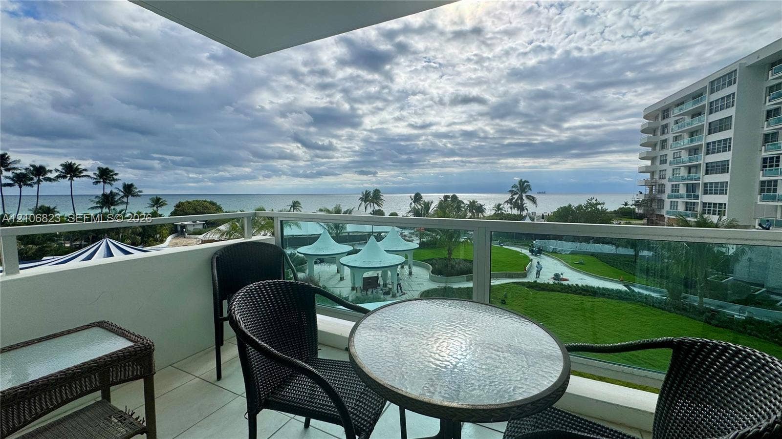 Covered balcony featuring glass paneled railings, white tile flooring, and direct oceanfront scenery