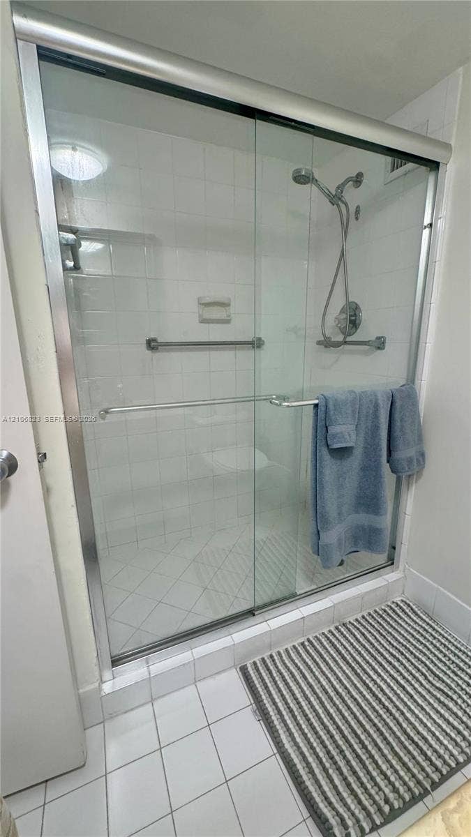 Walk-in shower enclosure featuring a sliding glass door, chrome hardware, adjustable hand-held shower head, and white wall tile