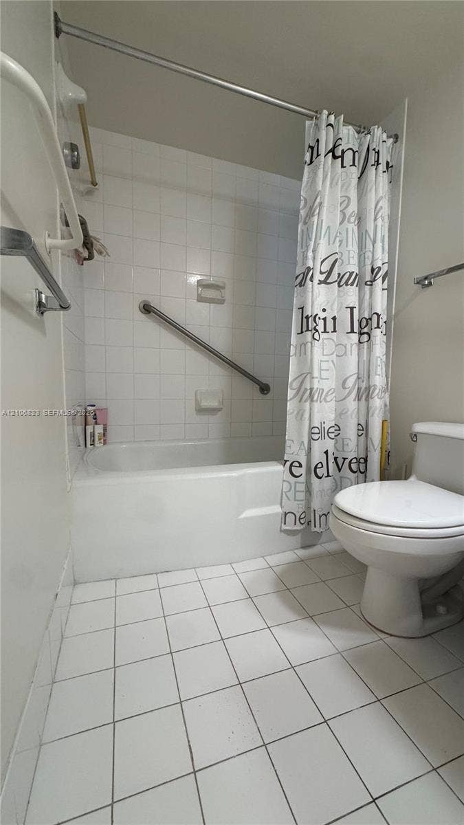 Full bathroom featuring a tub-shower combination with white tile surround, integrated metal grab bar, chrome fixtures, and white floor tile