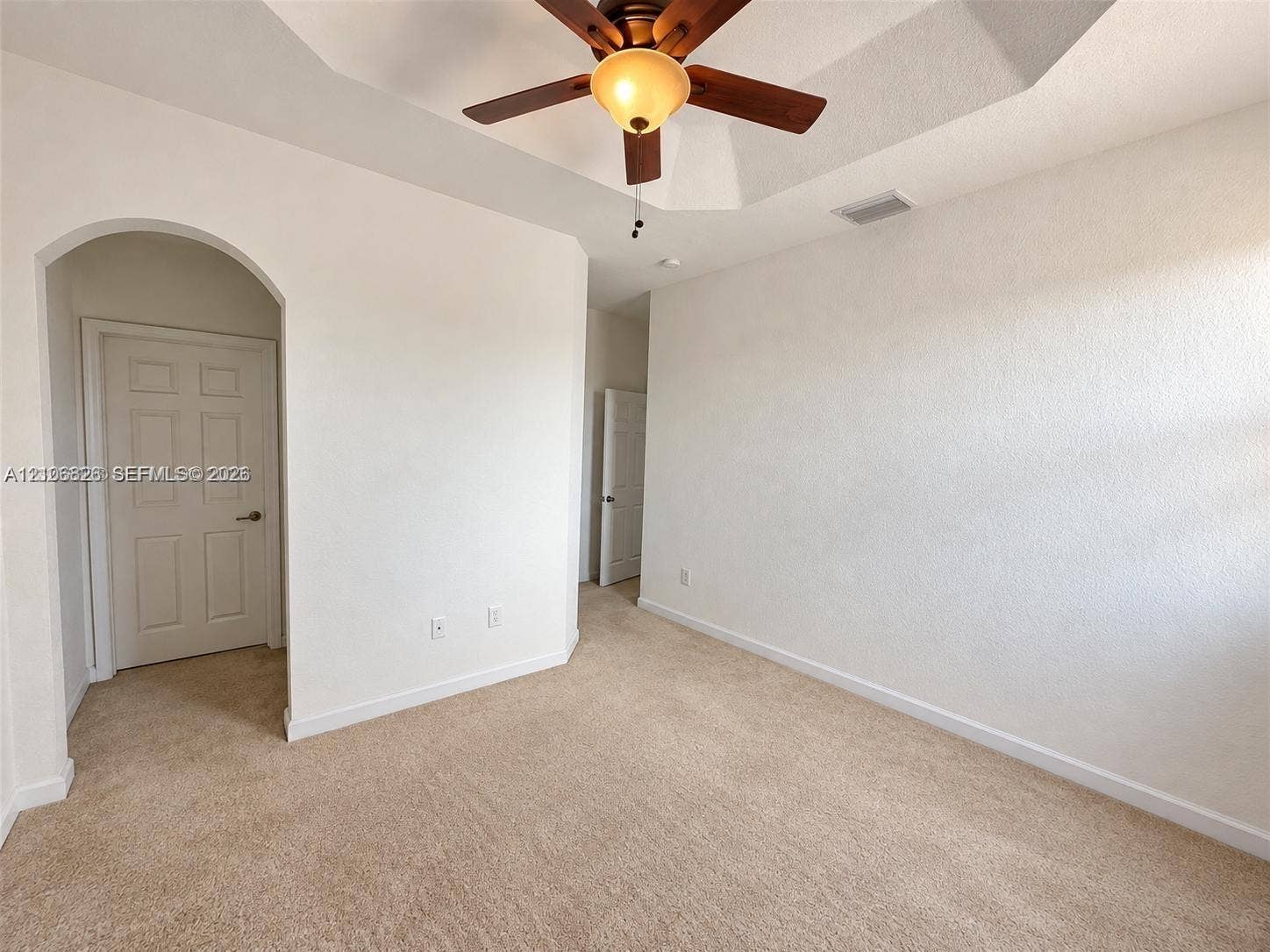 Tray ceiling, recessed lighting, central ceiling fan, arched doorway, and neutral wall-to-wall carpeting