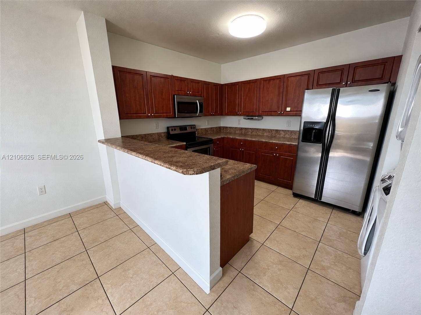 Kitchen featuring wood cabinetry, stone-finish countertops, stainless steel refrigerator, over-the-range microwave, and ceramic tile flooring