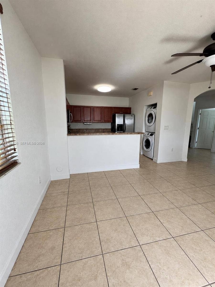 Kitchen featuring wood cabinetry, stone-finish countertops, stainless steel refrigerator, and tiled flooring, with a stacked laundry unit