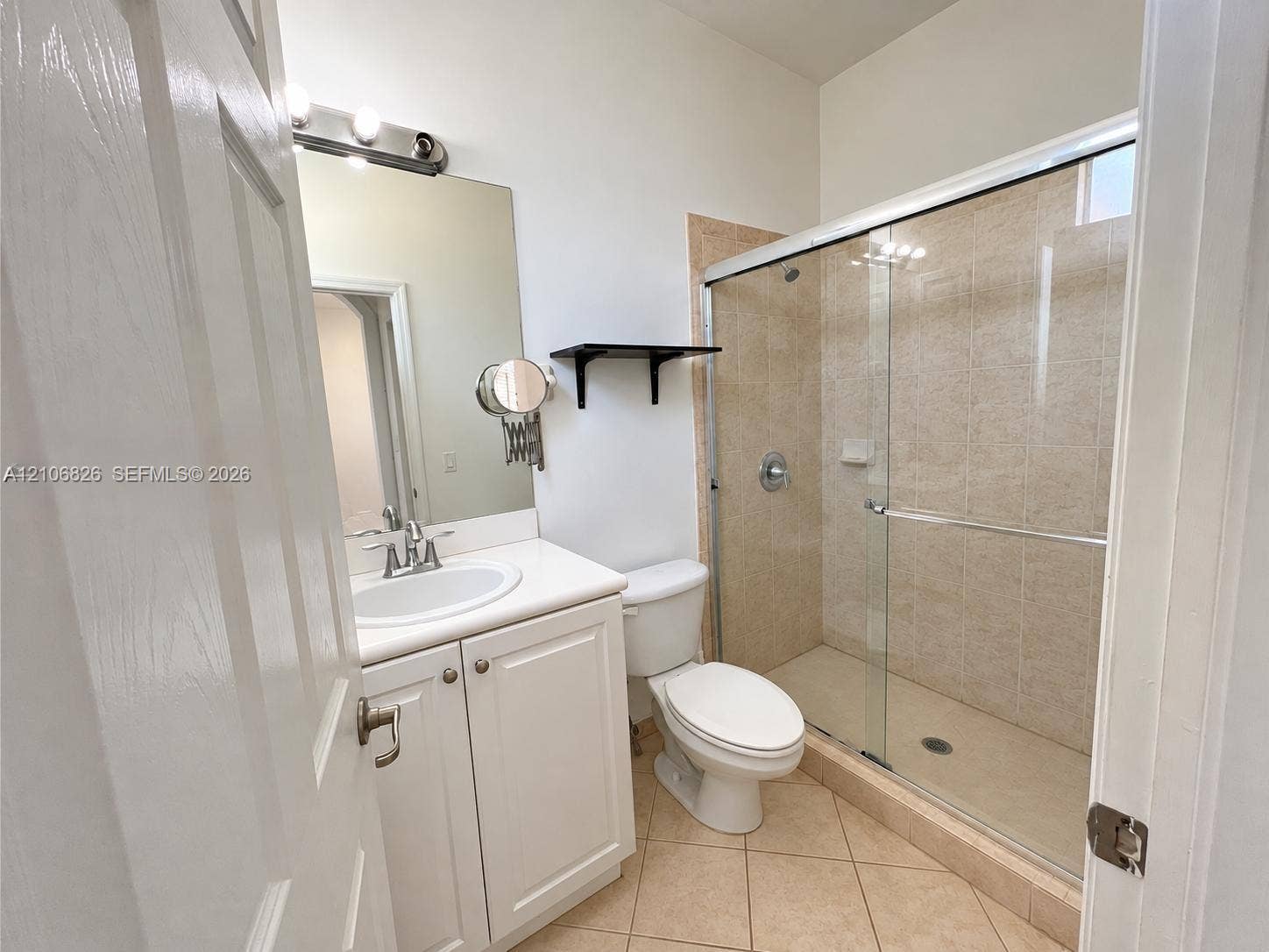 Bathroom featuring white vanity cabinetry, integrated sink, framed glass shower enclosure, tiled shower walls, and tile flooring