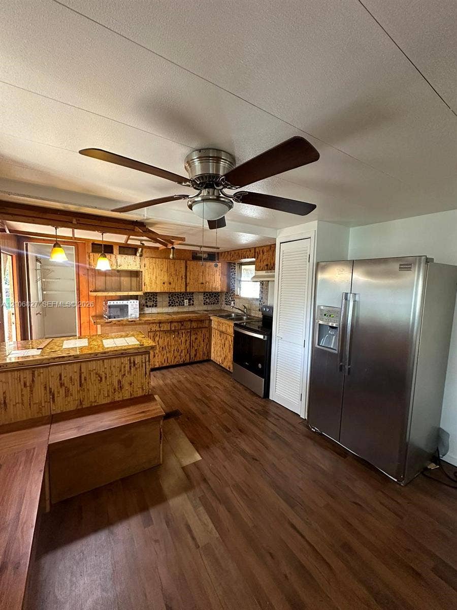 Kitchen featuring wood-finish cabinetry, tile backsplash, stainless steel side-by-side refrigerator, peninsula counter, and wood-finish flooring
