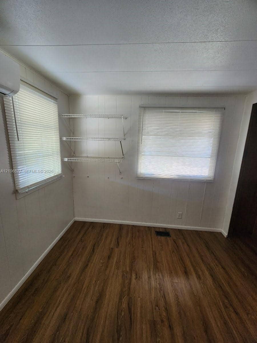 Wood-finish flooring, two windows with horizontal blinds, and three tiers of white wall-mounted wire shelving