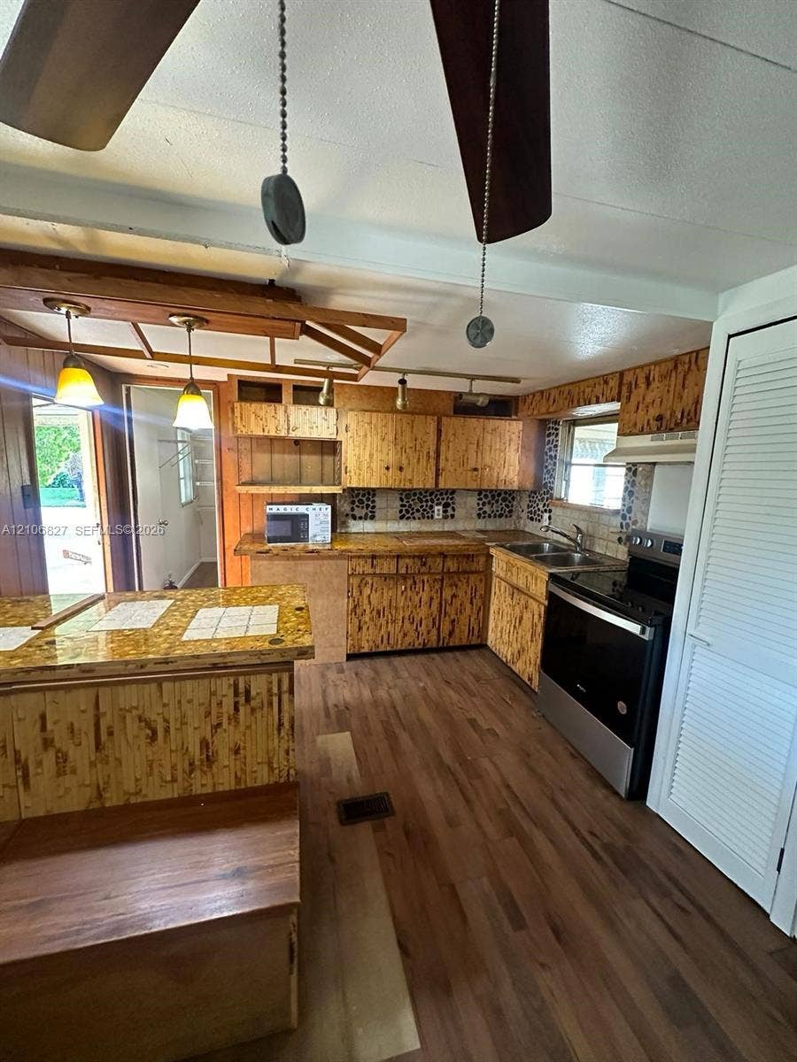 Kitchen featuring wood-finish flooring, wood cabinetry, stone-texture tile backsplash, a tiered peninsula counter, and recessed track lighting