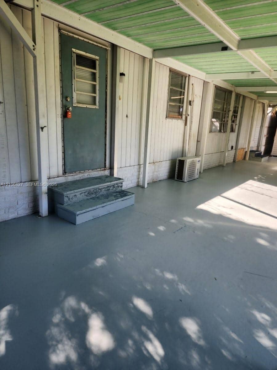 Covered exterior porch featuring vertical siding, painted concrete flooring, a paneled door with an integrated window, and built-in exterior lighting