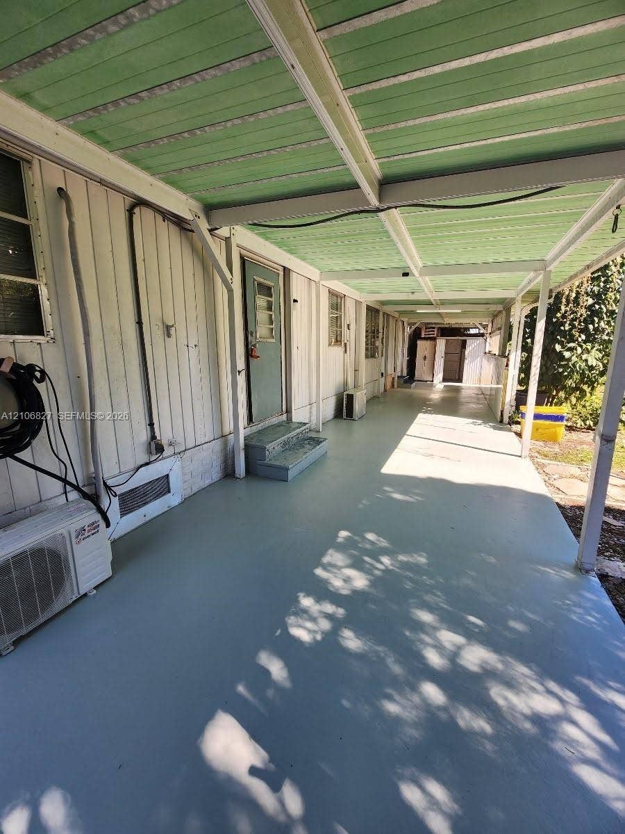 Covered exterior walkway featuring a painted concrete floor, vertical panel siding, and a green corrugated metal roof structure