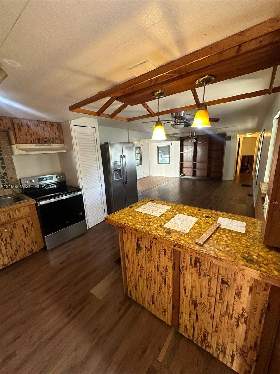 Kitchen featuring wood-finish cabinetry, a textured island countertop, stainless steel appliances, and a suspended wooden light fixture
