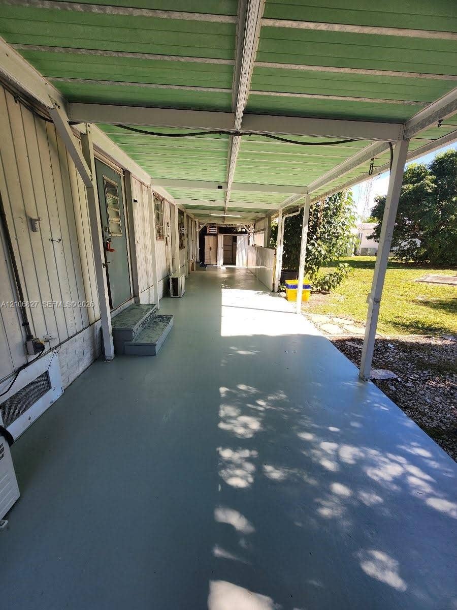 Covered exterior patio featuring a painted concrete floor, green corrugated metal roof, vertical exterior siding, and attached support pillars
