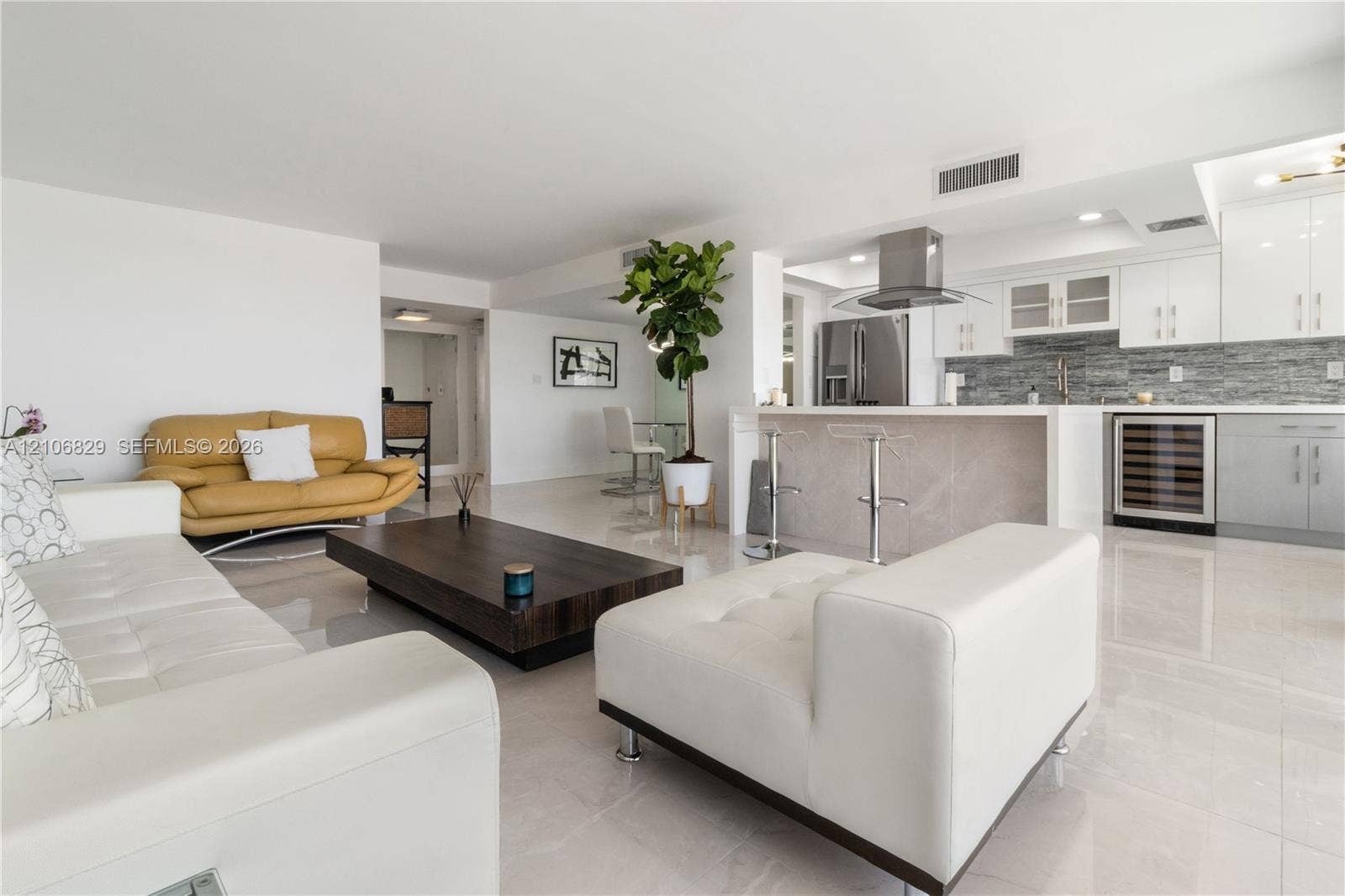 Open-concept living space featuring high-gloss tile flooring, white cabinetry, integrated stainless steel appliances, a kitchen island with a stone-finish facade, and a built-in wine refrigerator