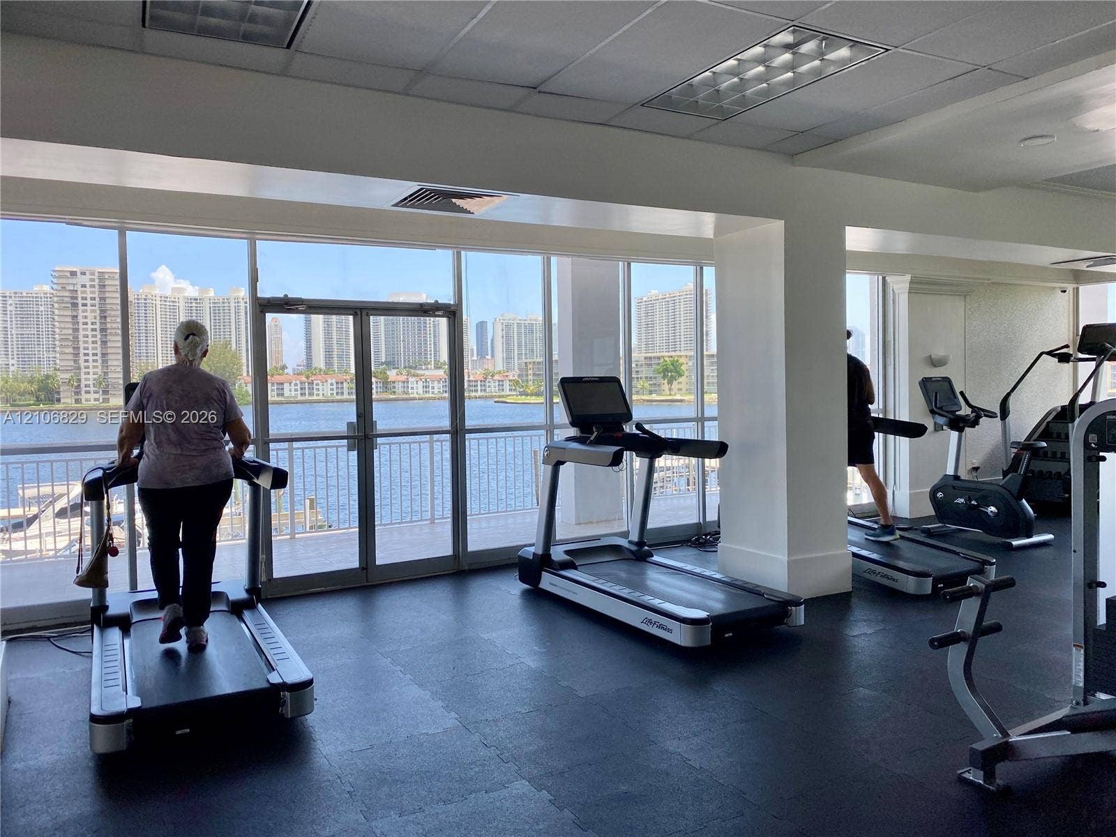 Fitness center featuring floor-to-ceiling glass windows, rubberized athletic flooring, recessed lighting, and water-facing exterior access doors