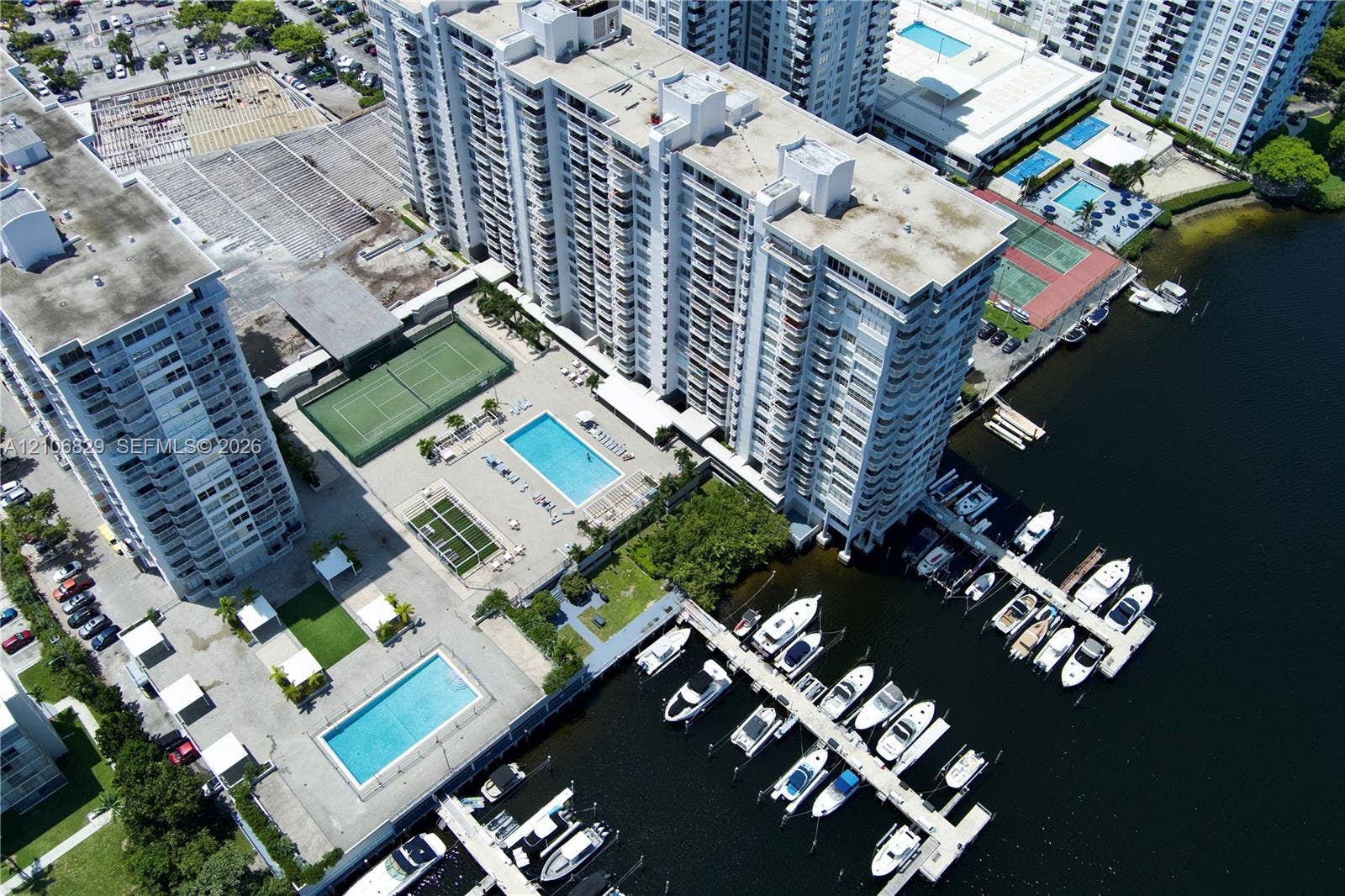 Aerial perspective of a multi-story residential complex featuring deep-water boat slips, two outdoor swimming pools, and tennis courts