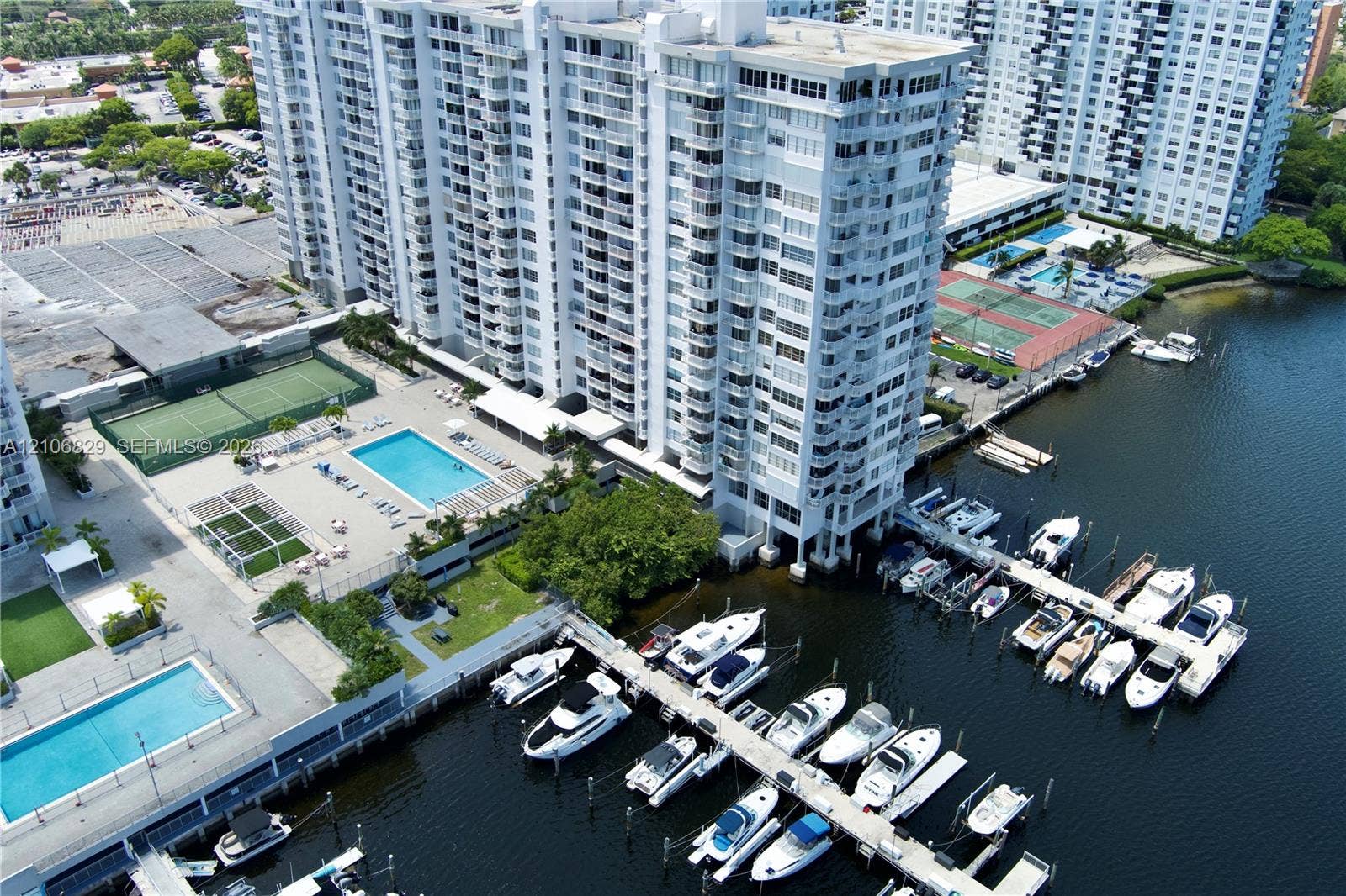 Aerial perspective of high-rise complex featuring an on-site marina with boat slips, multiple swimming pools, and a tennis court