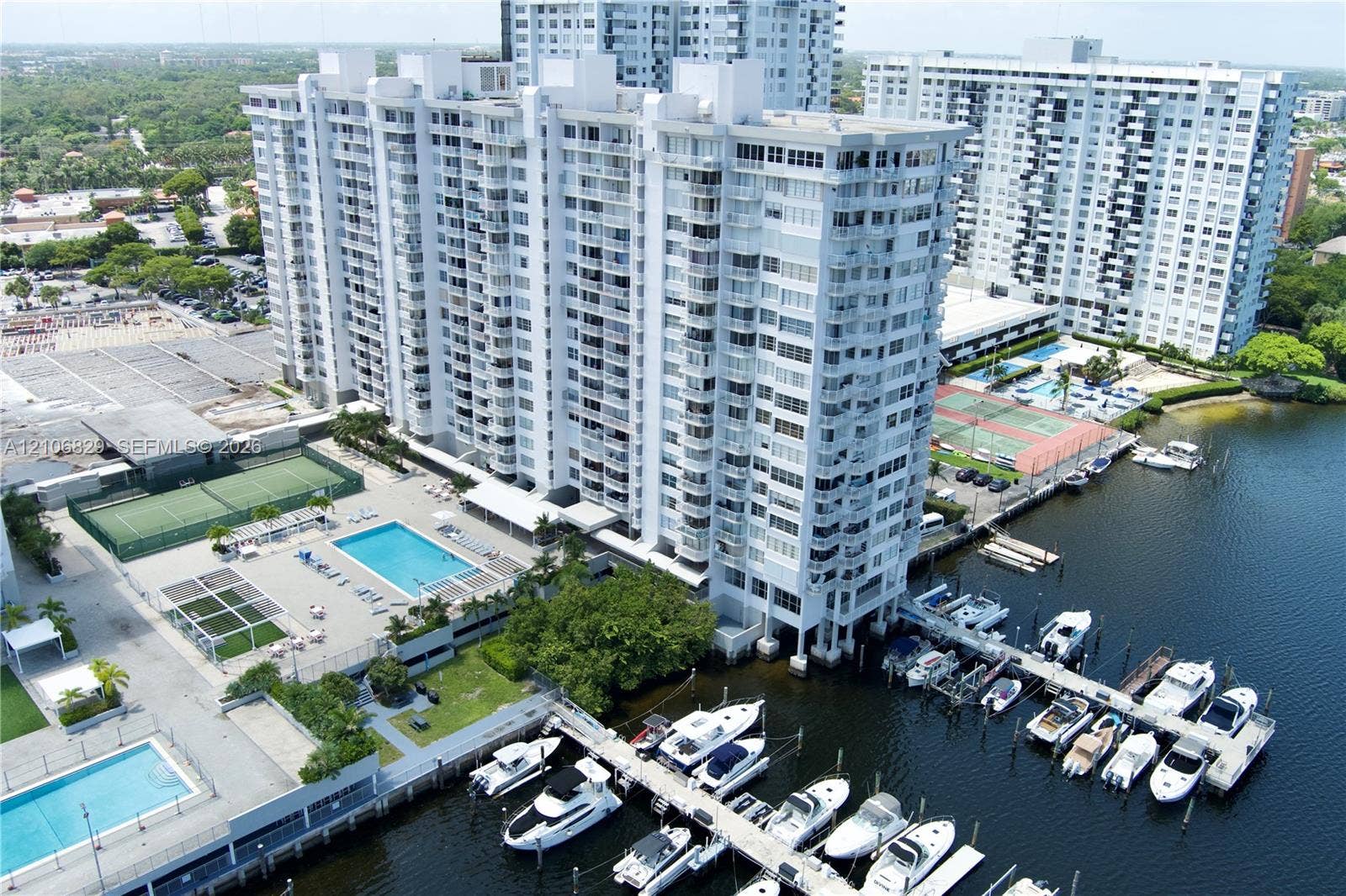 High-rise building exterior featuring private boat slips, multiple swimming pools, and tennis courts on the grounds