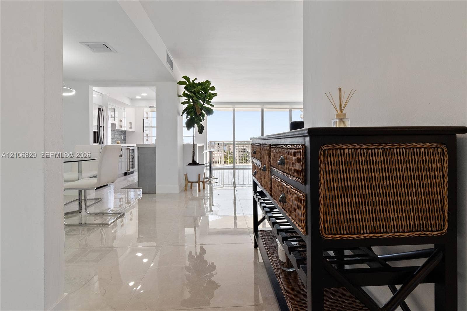 Polished tile flooring, floor-to-ceiling glass wall, and kitchen featuring white cabinetry and stainless steel appliances