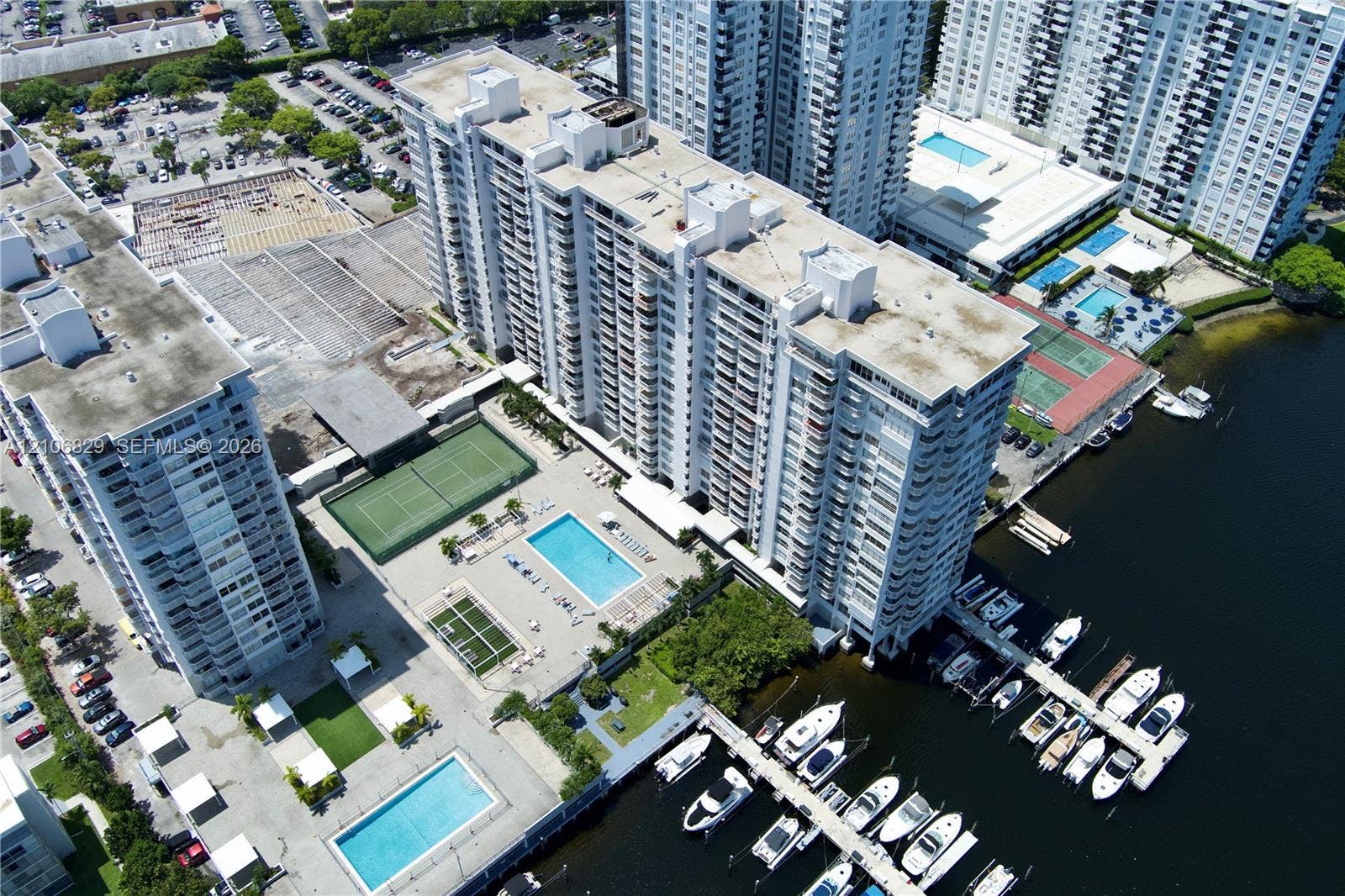 High-rise residential complex featuring waterfront boat slips, multiple outdoor swimming pools, tennis courts, and covered parking facilities