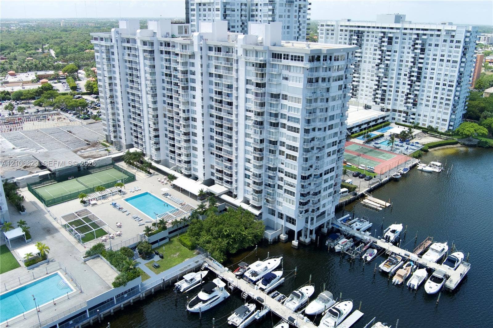 High-rise residential building featuring an on-site marina with boat slips, multiple outdoor swimming pools, and tennis courts situated on a waterfront property