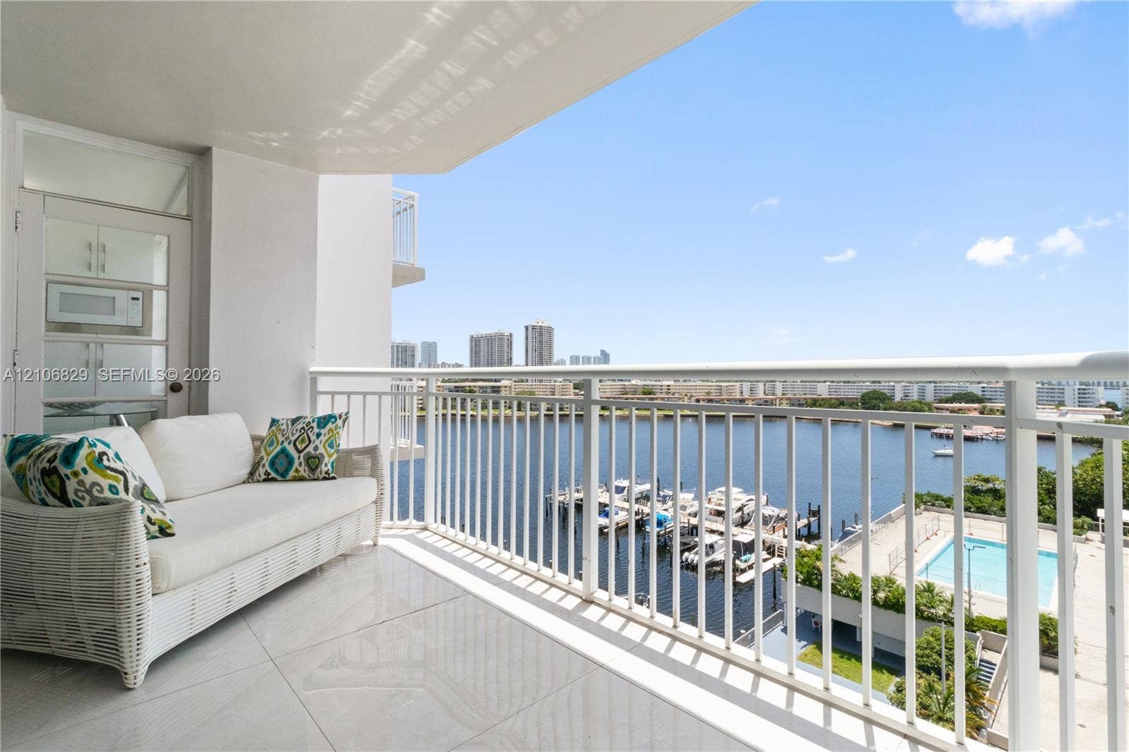 Covered balcony featuring large-format tile flooring and a white metal railing overlooking a marina and waterway