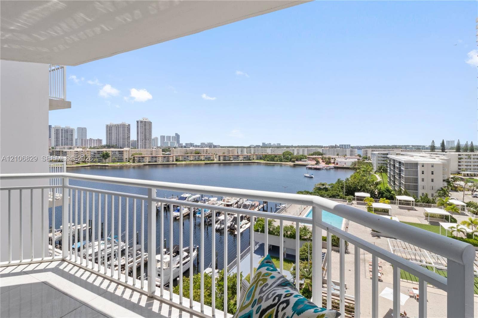 Private balcony featuring white metal railings, tile flooring, and direct water exposure with views of the marina and skyline