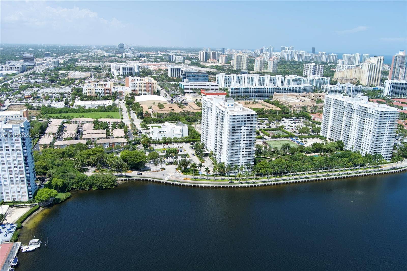 Aerial perspective of waterfront high-rise residential buildings featuring manicured perimeter landscaping, tennis courts, and direct bulkhead access to the waterway