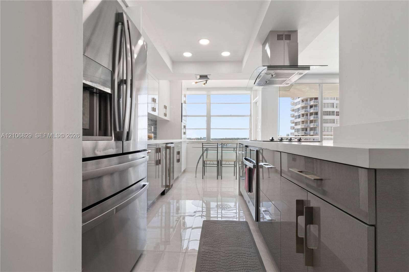 Kitchen featuring high-gloss cabinetry, stainless steel appliances, a stainless steel range hood, quartz countertops, and polished tile flooring