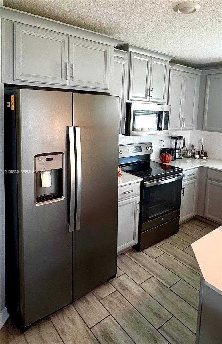 Kitchen featuring shaker-style cabinetry, stainless steel appliances, white solid-surface countertops, and wood-finish tile flooring