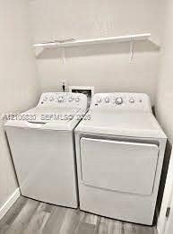 Laundry area featuring a top-loading washing machine, clothes dryer, and wall-mounted white shelving over wood-finish flooring