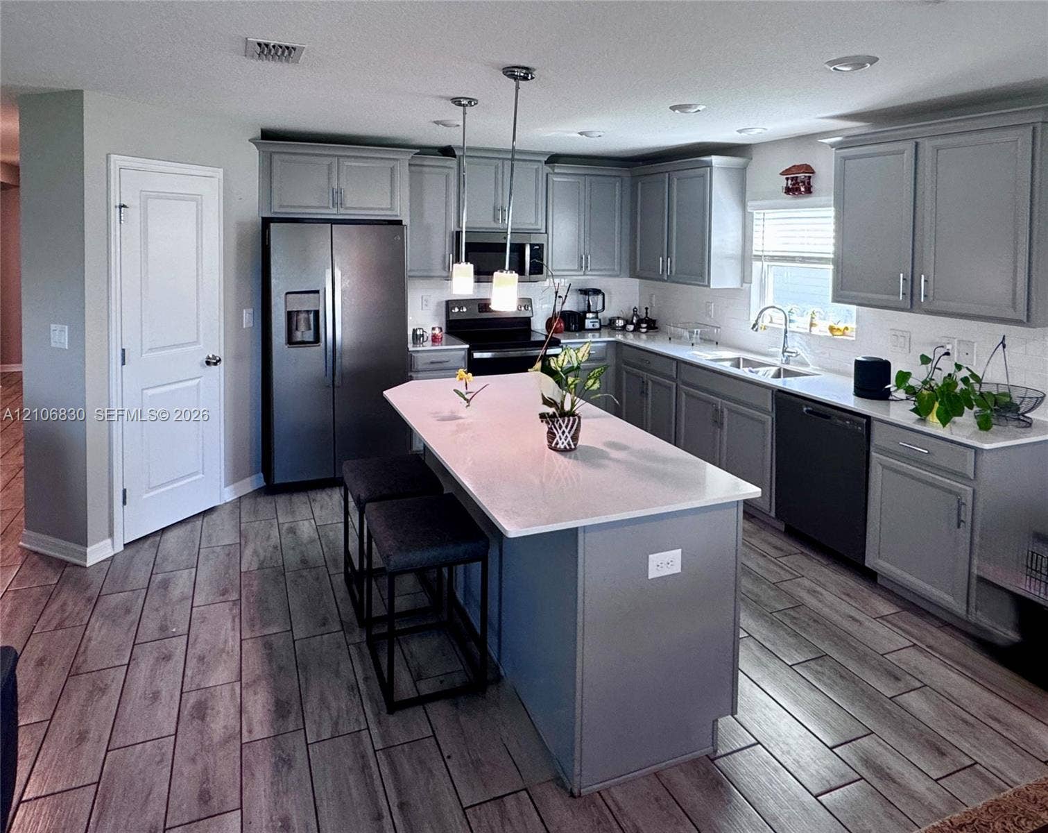 Kitchen featuring gray cabinetry, a central island with a solid surface countertop, wood-finish tile flooring, recessed lighting, and stainless steel appliances