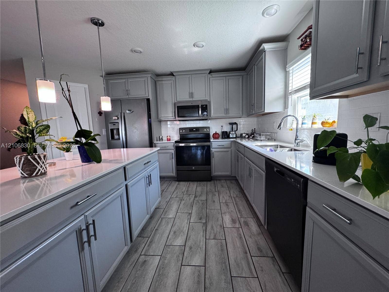 Kitchen featuring gray cabinetry, stone-finish countertops, subway tile backsplash, stainless steel appliances, and wood-finish flooring