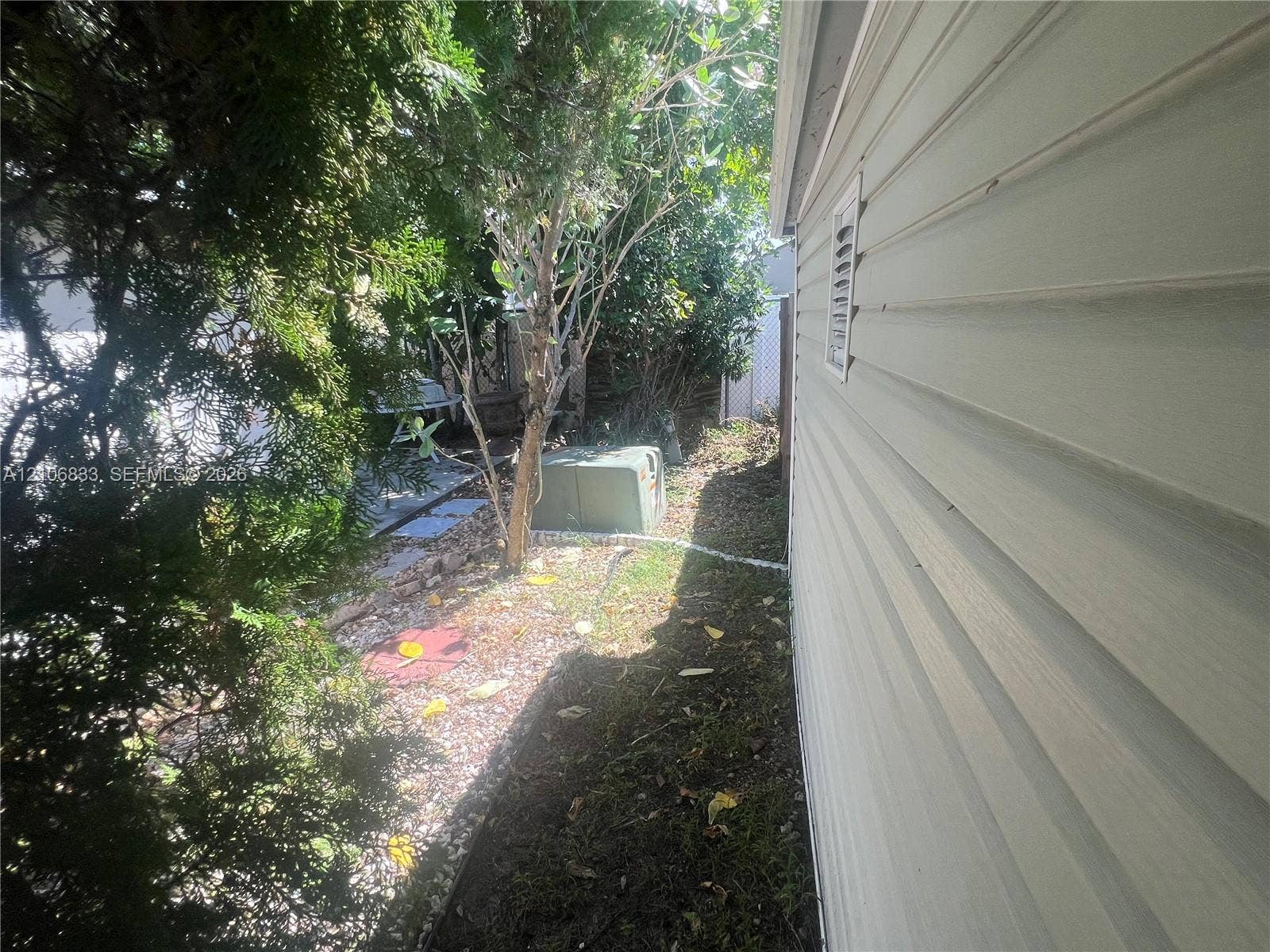 2782 E Marina Drive, Dania Beach, FL 33312 Light-colored horizontal siding, exterior utility enclosure, and landscaping featuring mature coniferous trees